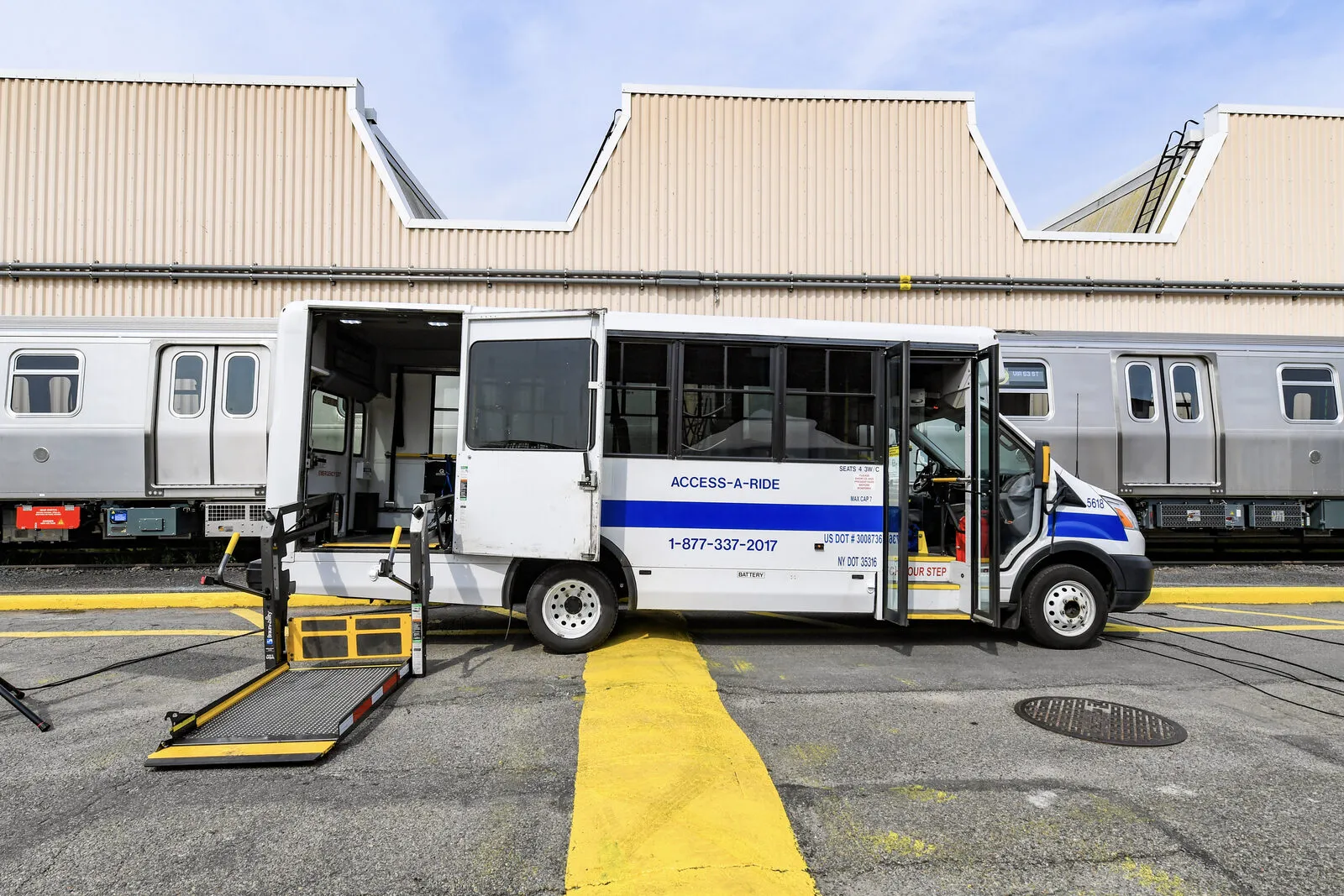 A white Access-A-Ride paratransit cutaway bus in New York, parked with its rear wheelchair lift lowered to the ground and its doors open