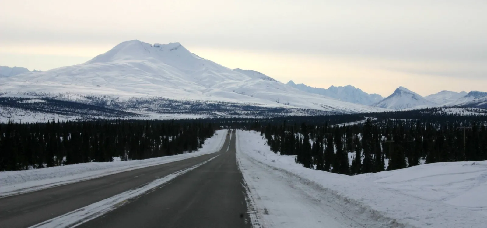 The snowy Glenn Highway running straight through spruce forest toward Gunsight Mountain in Southcentral Alaska