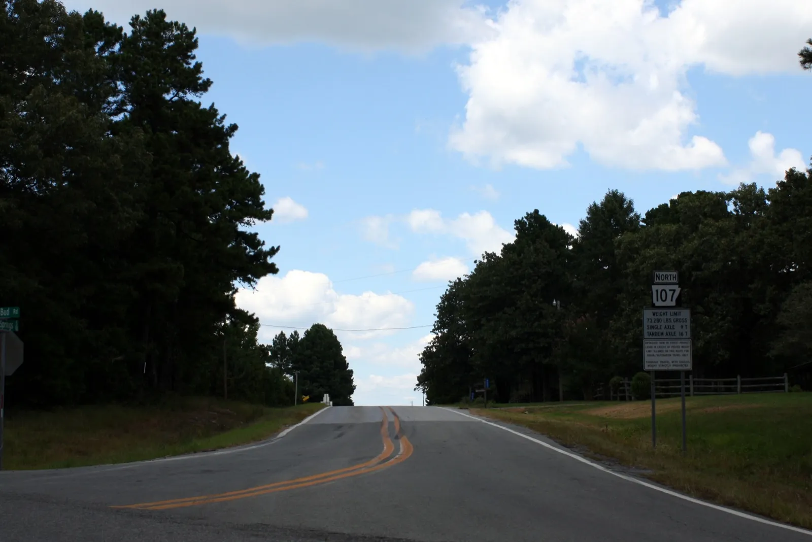 A two-lane rural highway, Arkansas Highway 107, rising between pine trees under a blue sky in Cleburne County