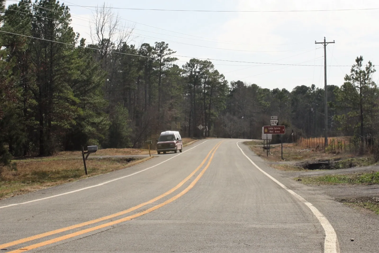 A high-top van on a two-lane road through pine woods, Arkansas Highway 324 near Williams Junction