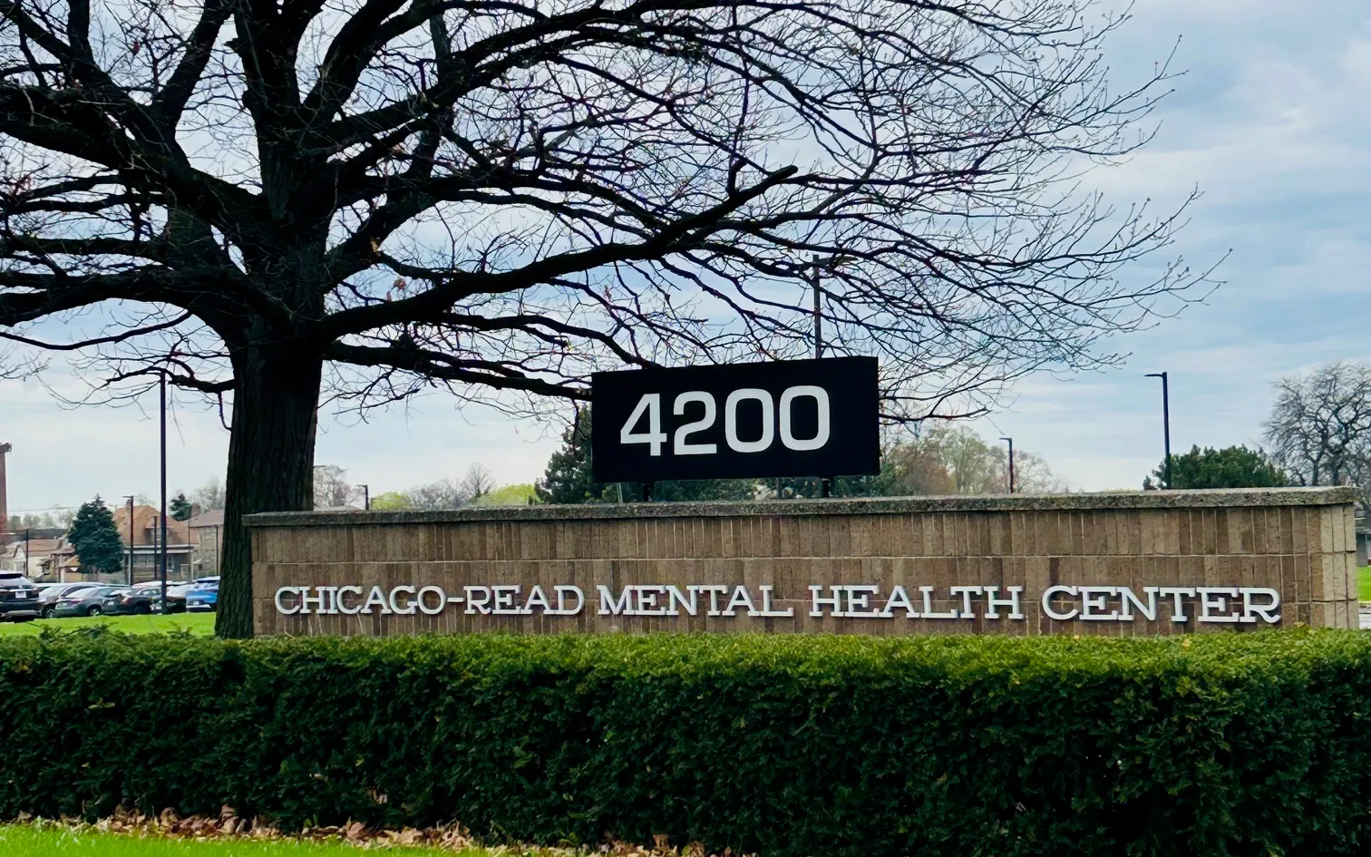 The brick entrance sign of the Chicago-Read Mental Health Center under a bare tree, behind a trimmed hedge