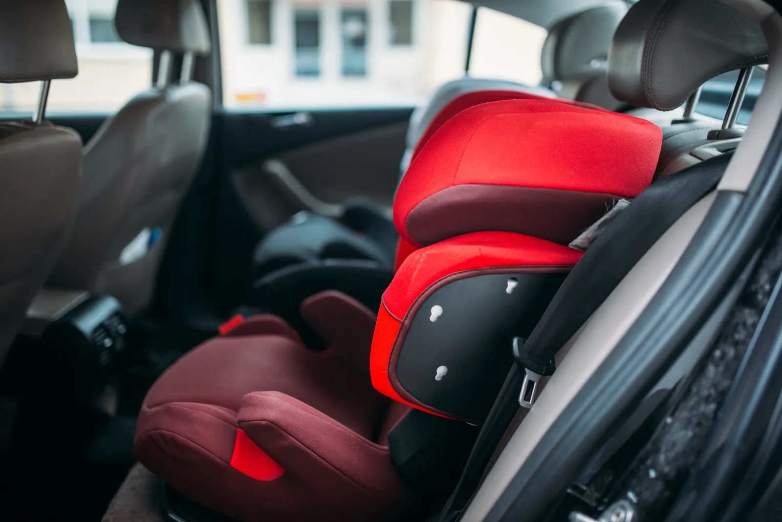 A red high-back child booster seat in the back seat of a car