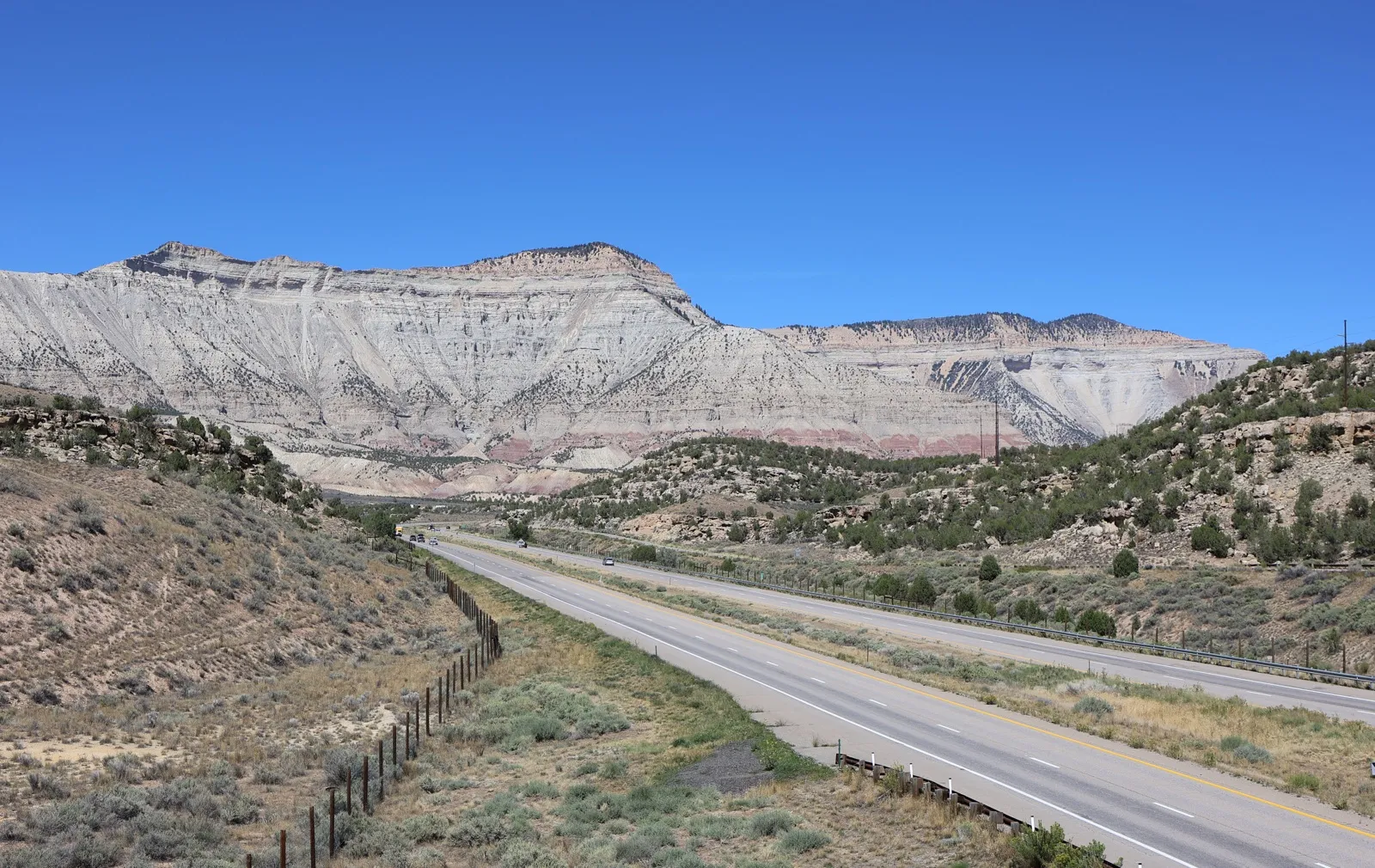 Interstate 70 curving through sagebrush hills below the pale Roan Cliffs in western Colorado under a clear blue sky