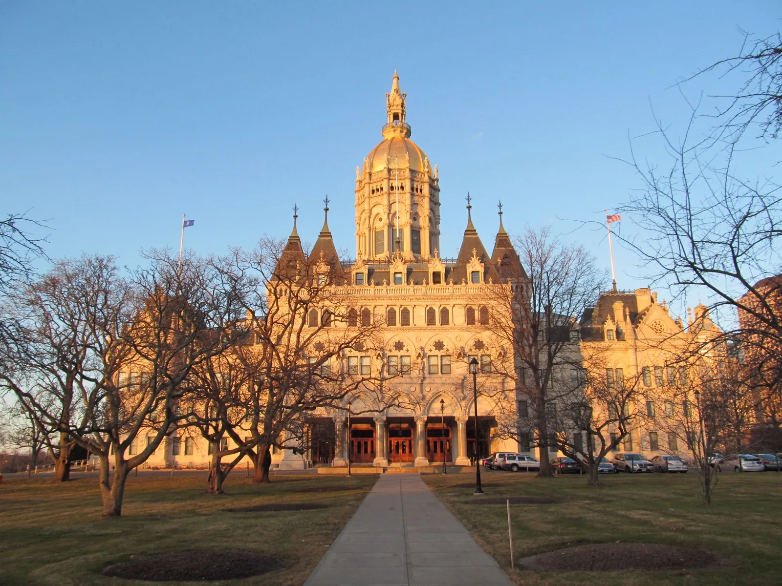 The Connecticut State Capitol in Hartford, its gold dome lit by low sun, seen past bare winter trees