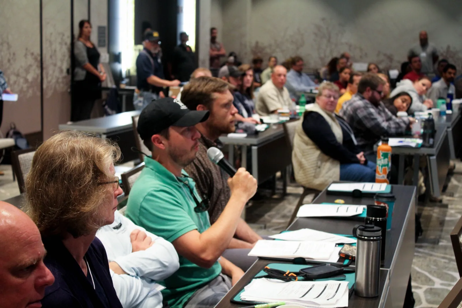 New employees seated at long tables in a training room, one asking a question into a microphone while the others listen