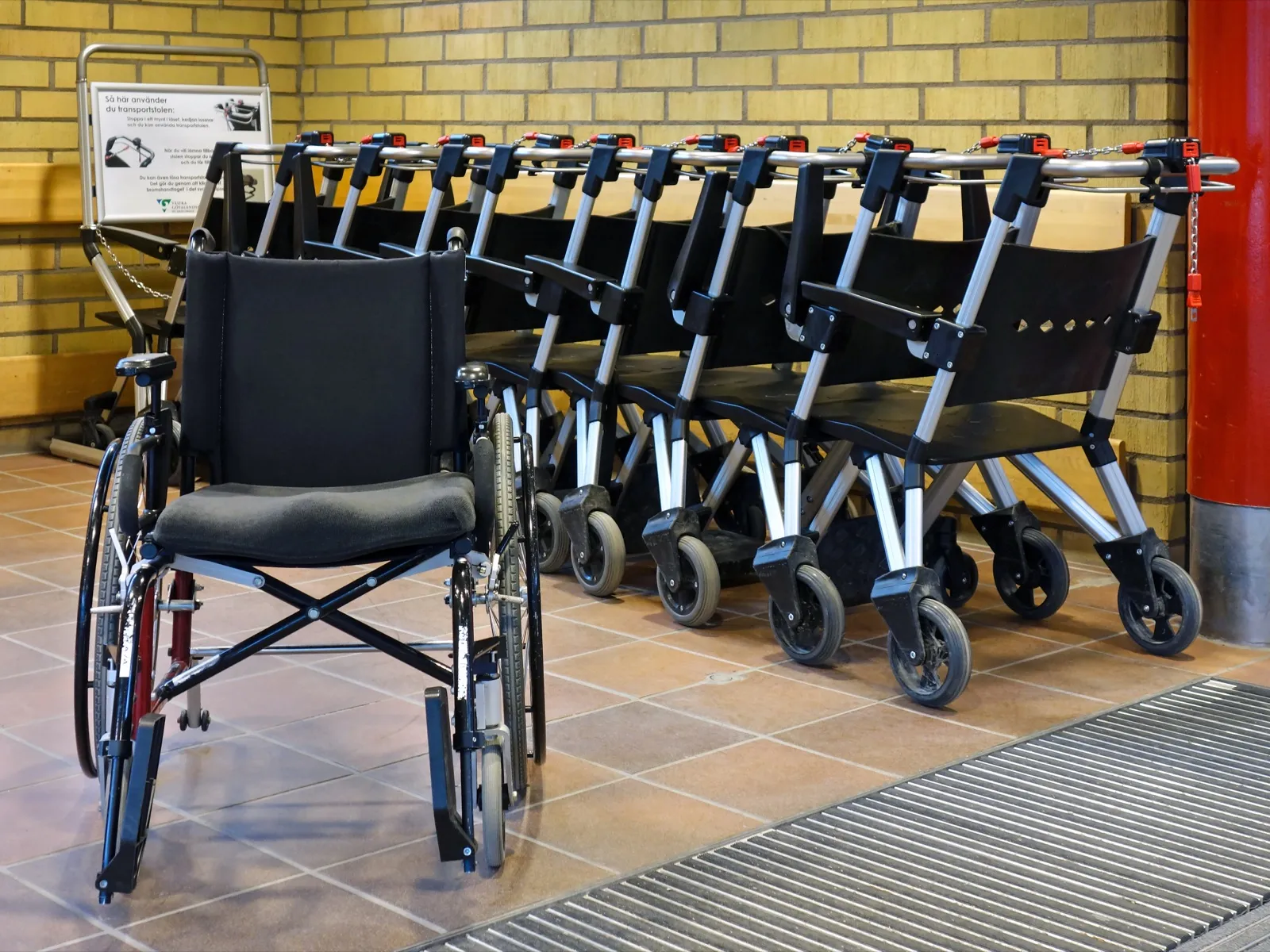 An empty wheelchair parked in front of a row of transport chairs at a hospital main entrance
