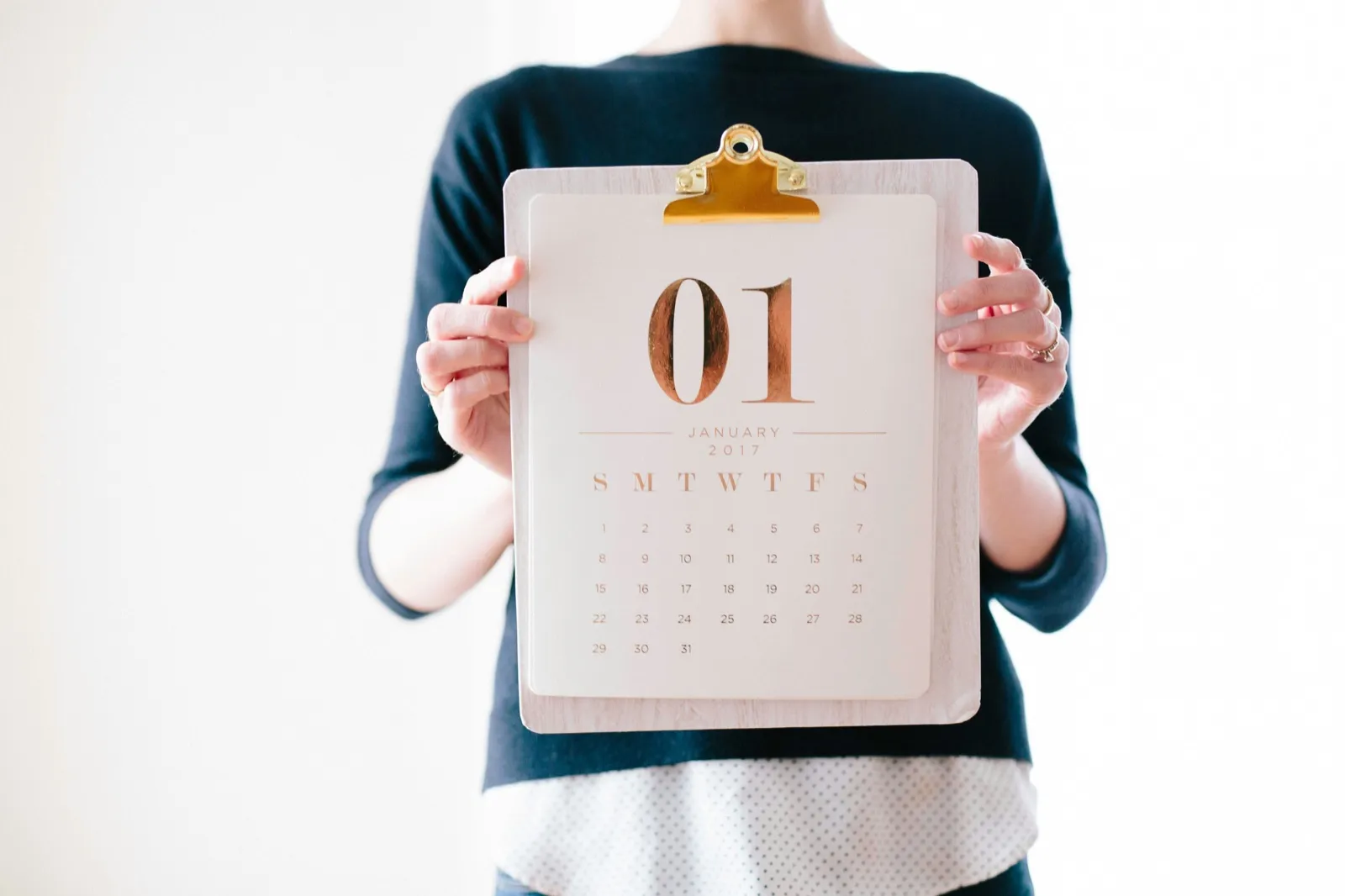 A person holding a clipboard with a one-month paper calendar clipped to it