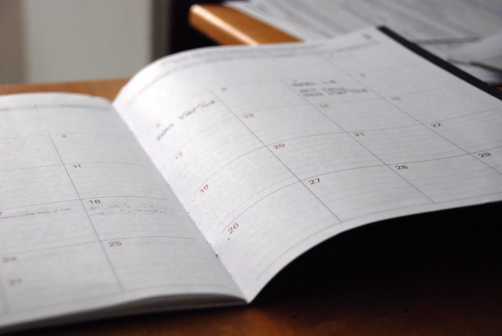 An open monthly planner on a wooden desk, with a few handwritten notes in the date boxes