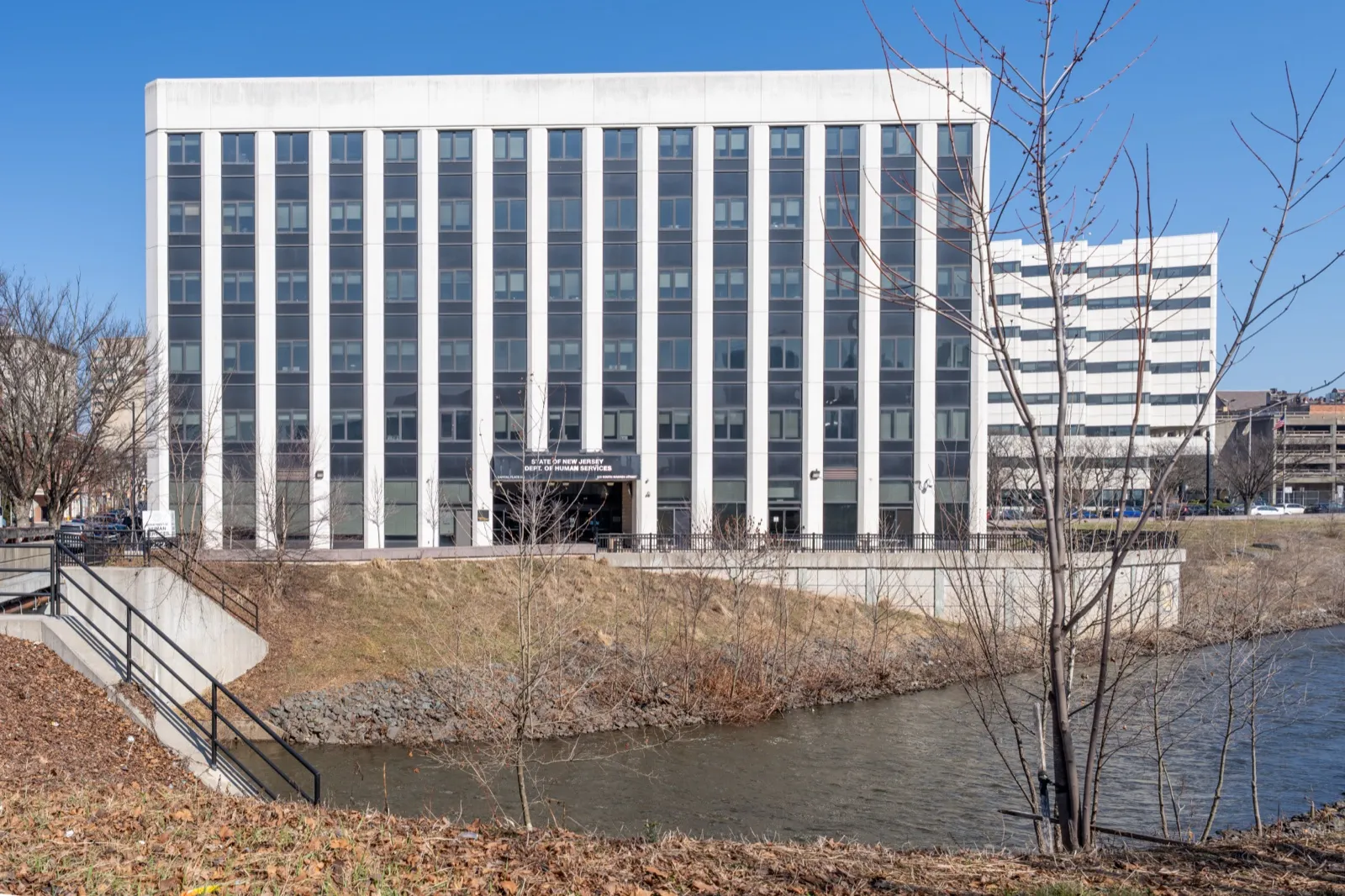 The State of New Jersey Department of Human Services building in Trenton, a white office block beside a creek under a clear blue sky