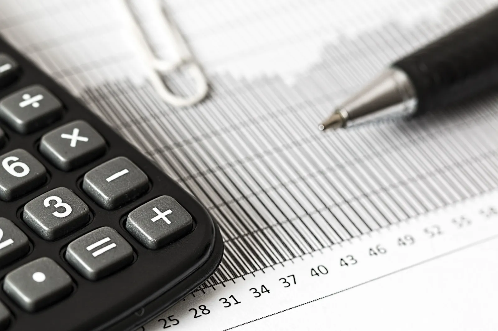 Close-up of a calculator and a ballpoint pen resting on a printed bar chart