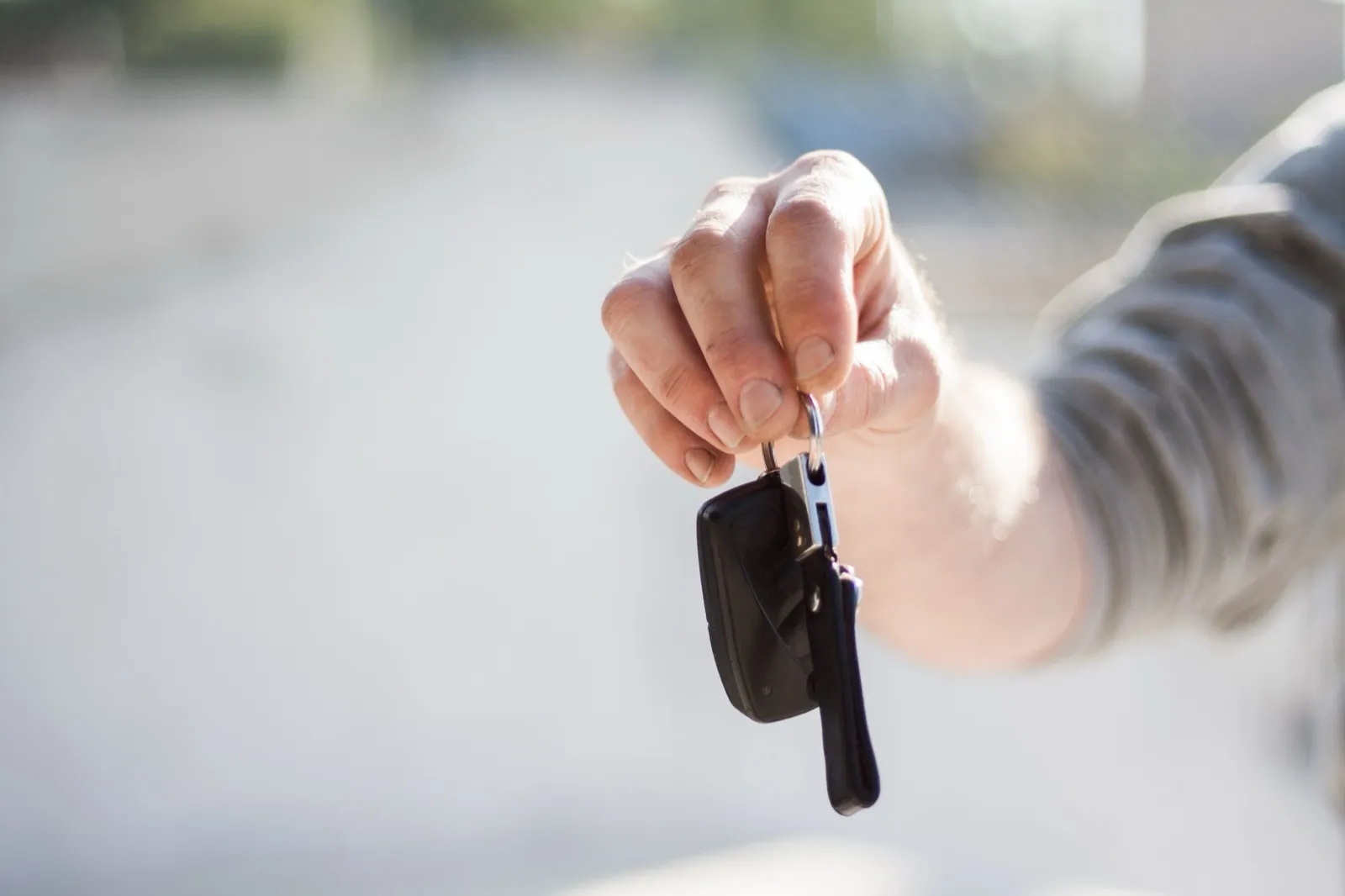 A hand holding out a set of car keys, as if passing them to a new owner