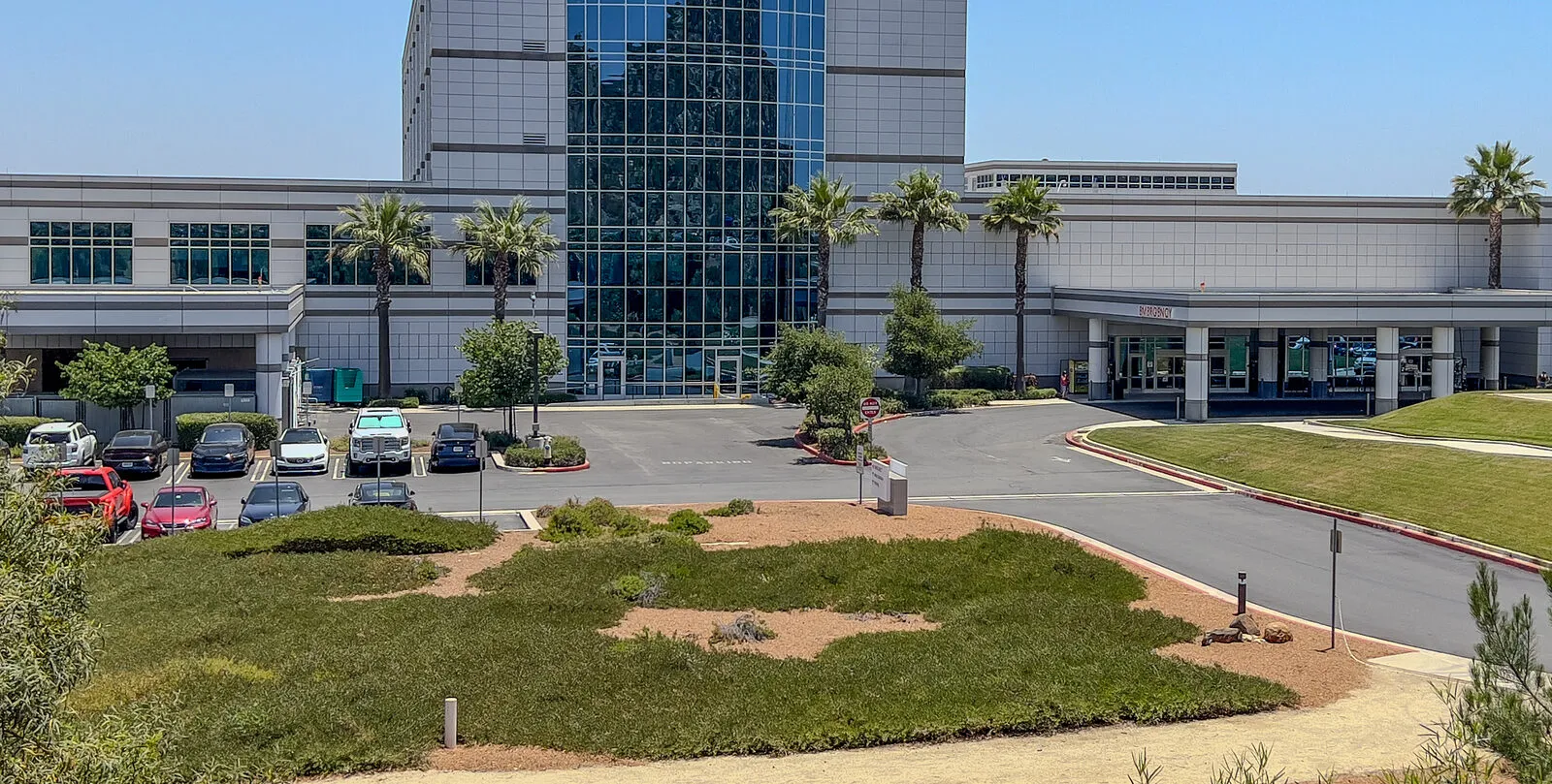The front drive and emergency entrance of a glass and white hospital in Murrieta, Riverside County, with palm trees and a parking lot