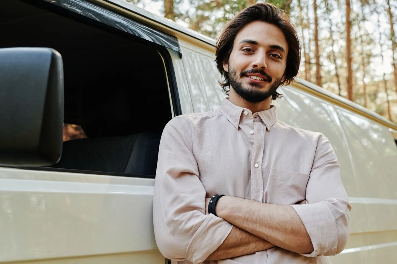 A smiling man in a light button-up shirt leans with his arms crossed against the side of a white van