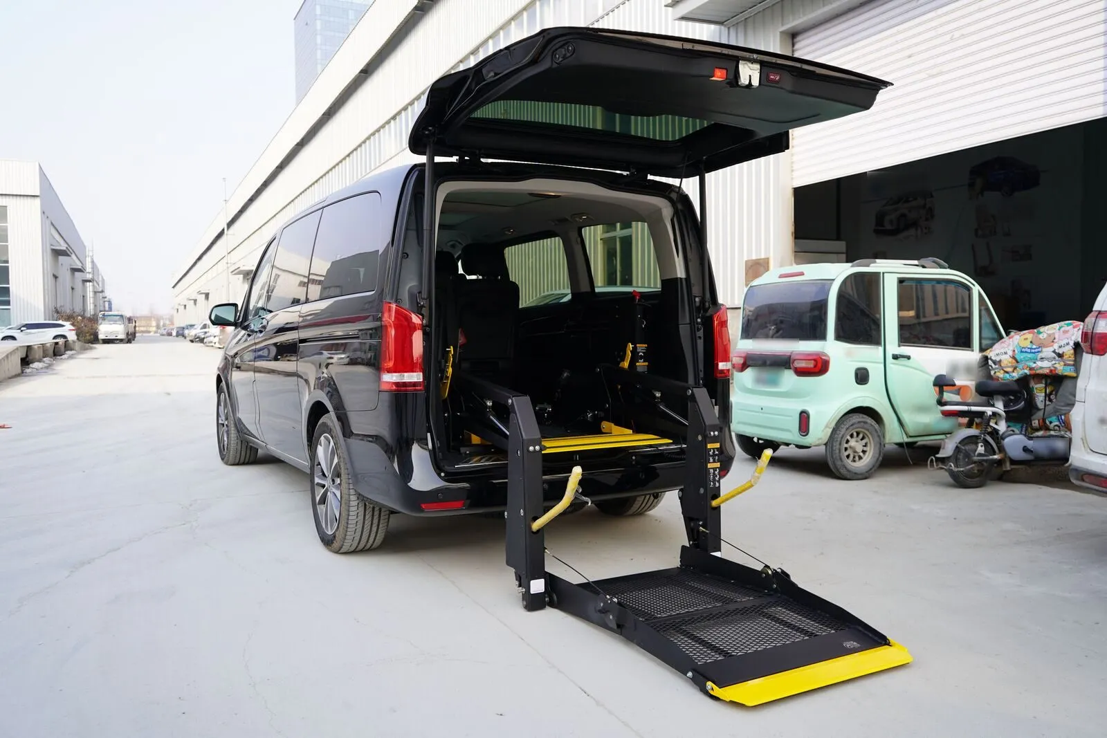 A black passenger van with its rear hatch raised and a wheelchair lift lowered to the pavement behind it