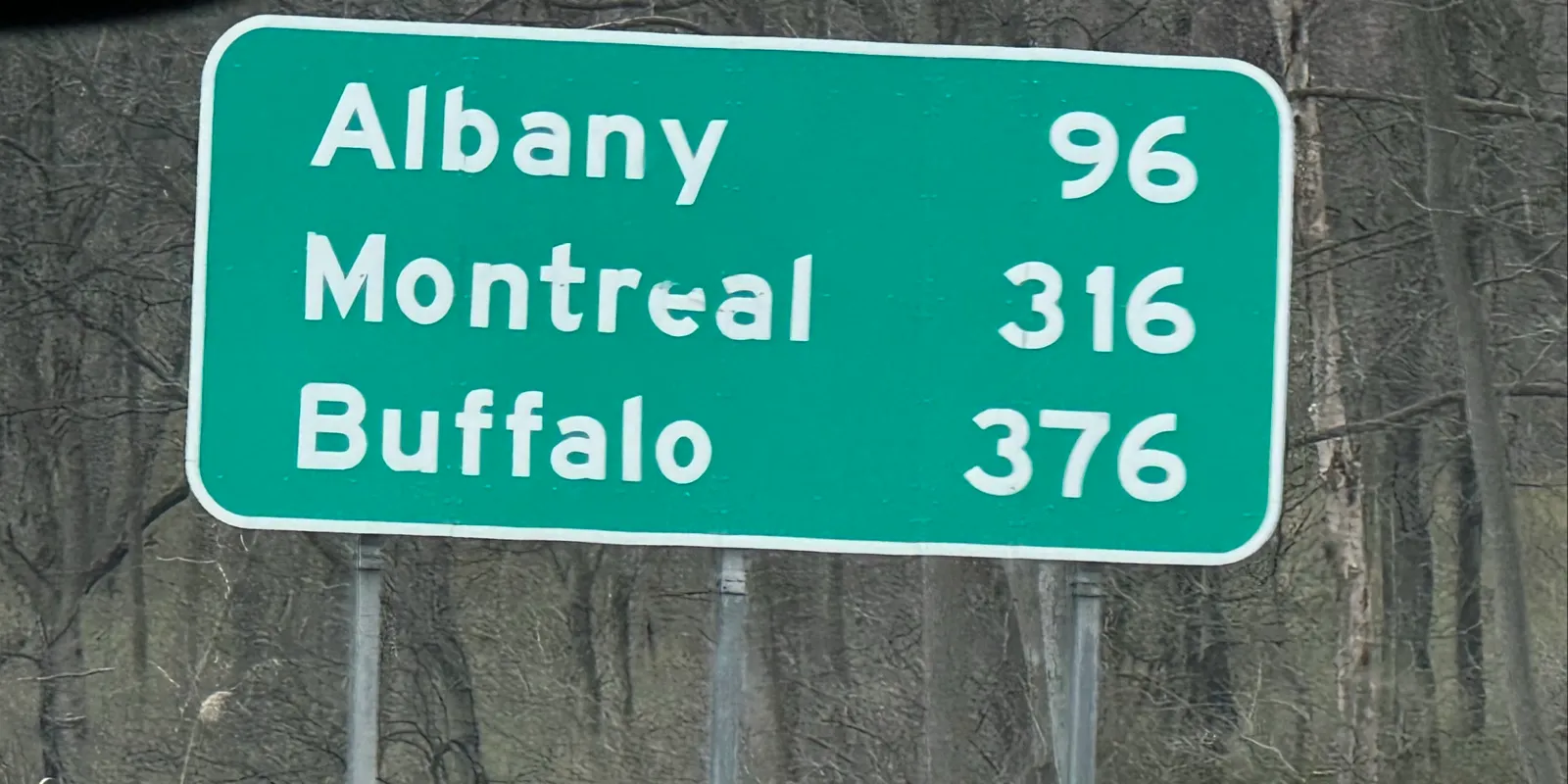 A green highway mileage sign on the New York State Thruway listing Albany 96, Montreal 316, and Buffalo 376 miles