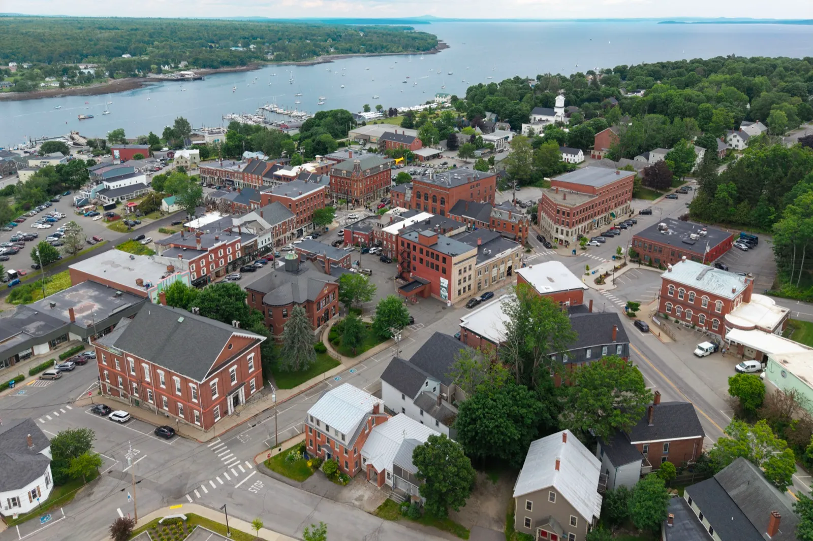 Aerial view of downtown Belfast, Maine, with brick buildings, parked cars, and the harbor beyond