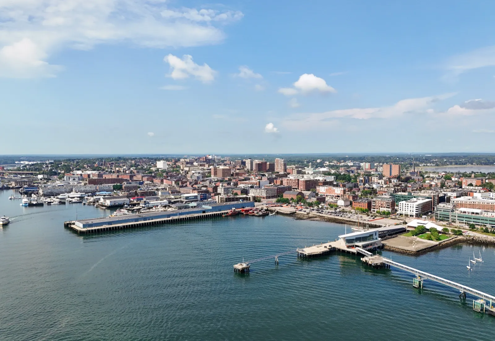 Aerial view of Portland, Maine: the downtown skyline, the waterfront piers, and the harbor under a blue sky