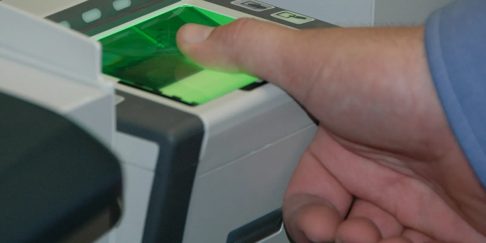 A finger pressed on the green-lit glass of a digital fingerprint scanner