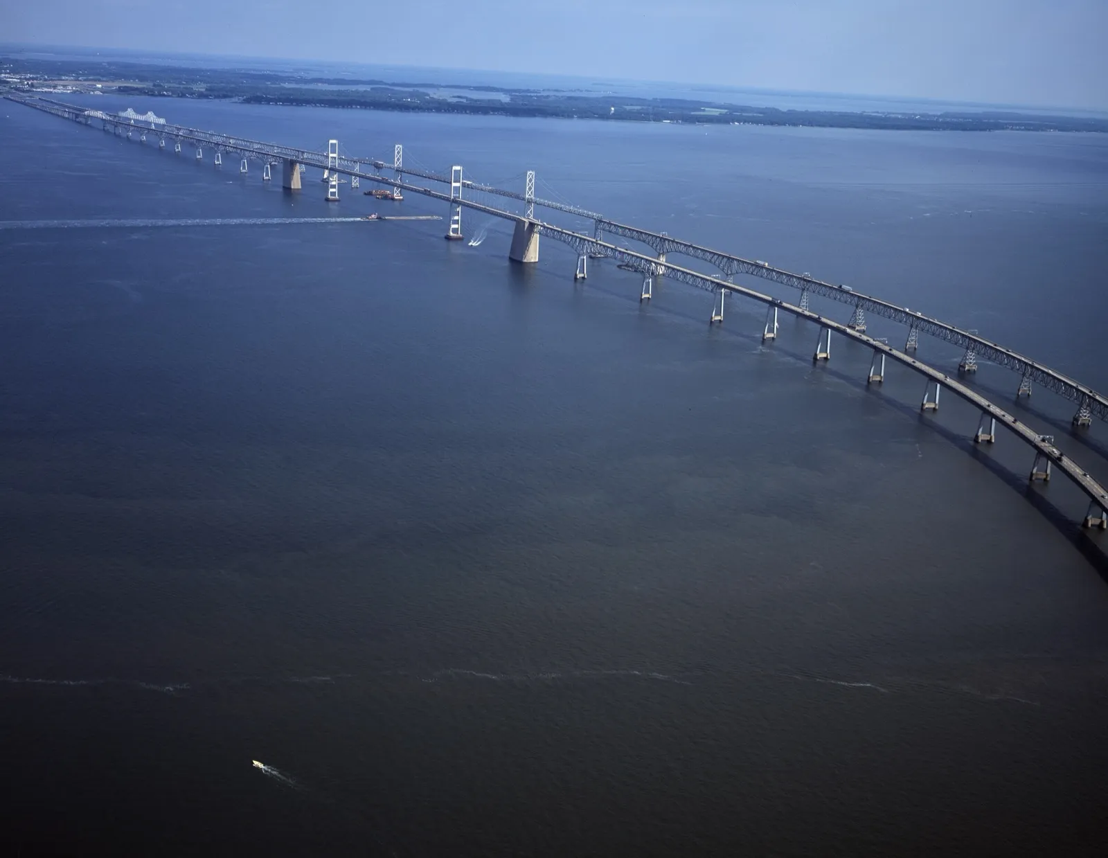 An aerial view of the twin spans of the Chesapeake Bay Bridge curving across the bay toward Maryland's Eastern Shore