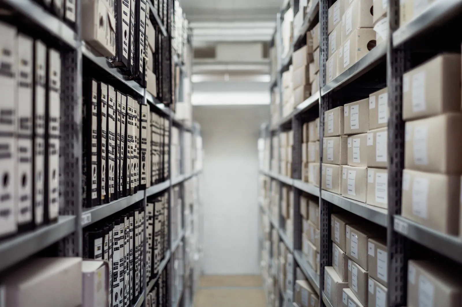 A long aisle of metal shelves filled with labeled archive boxes and black ring binders