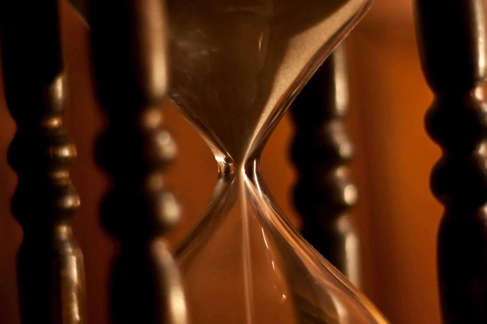 Close-up of a wooden hourglass with a thin stream of sand running through its narrow neck