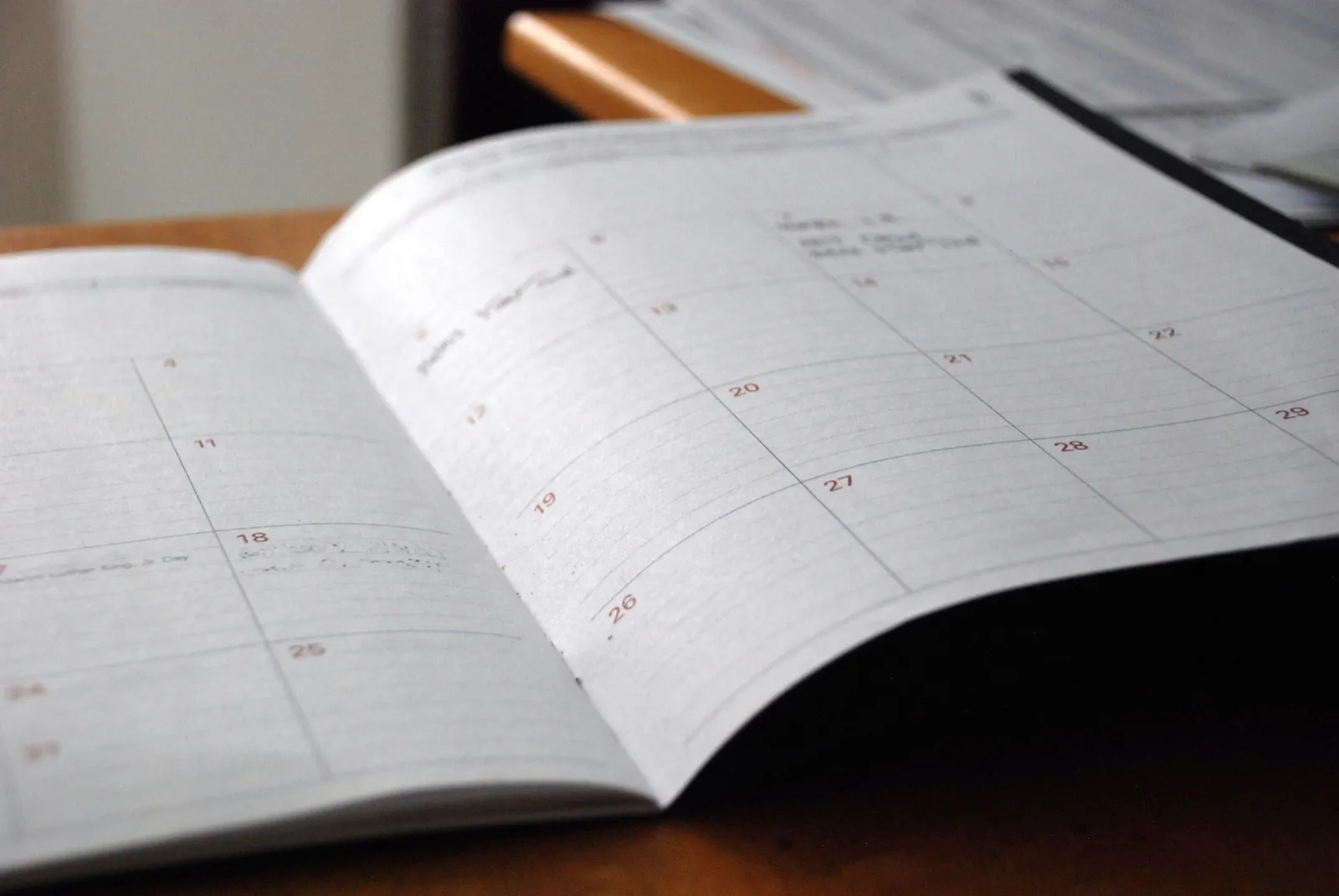 An open monthly planner lying on a wooden desk, its date grid mostly empty