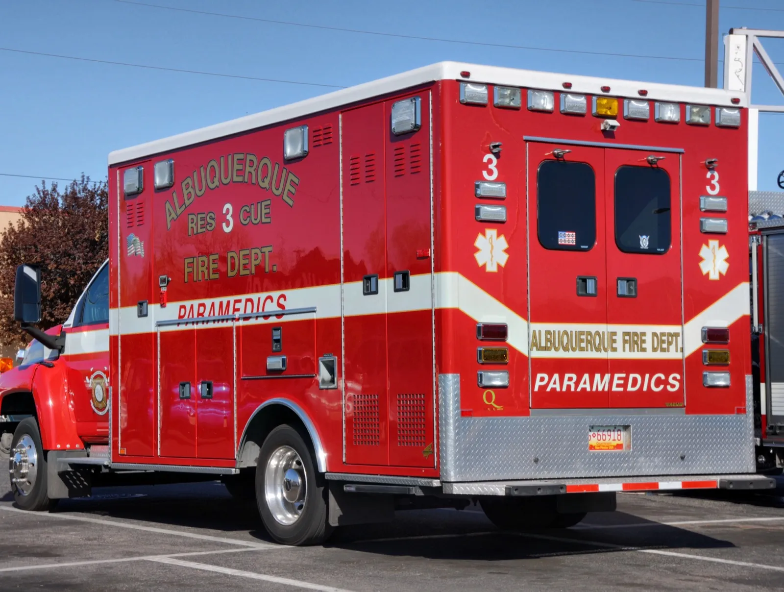 The back of a red fire department ambulance marked Paramedics, parked in a lot under a clear blue sky
