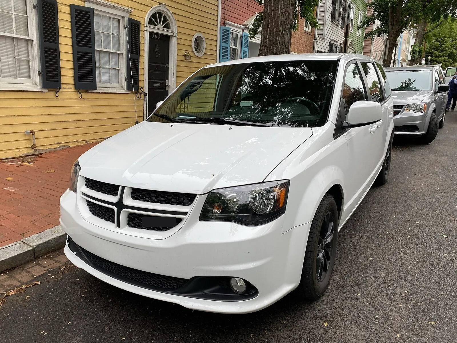 A white minivan parked at the curb of a residential street in front of a row of painted houses