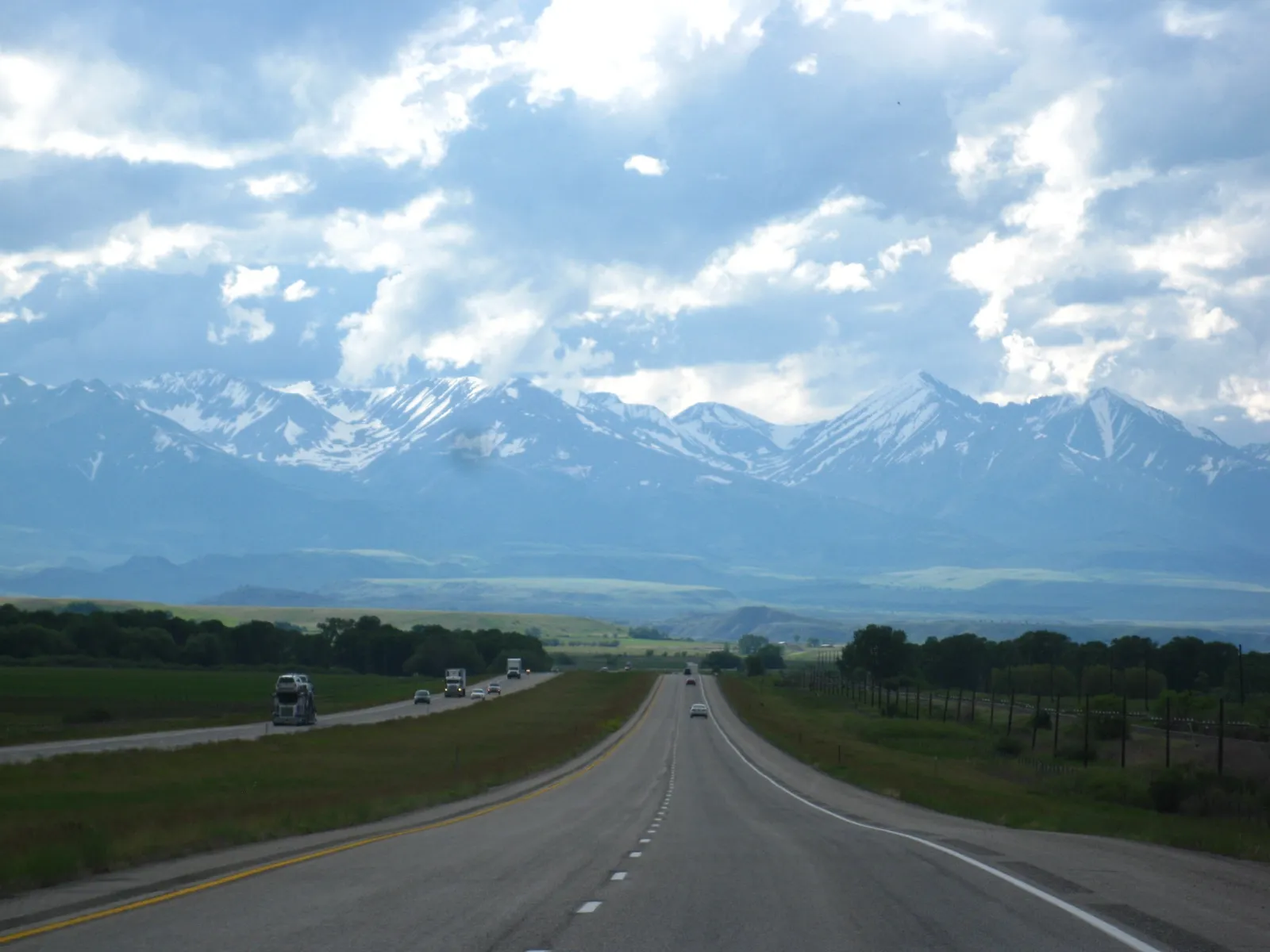 Interstate 90 near Park City, Montana, running between green fields toward snow-capped mountains under a wide, cloudy sky