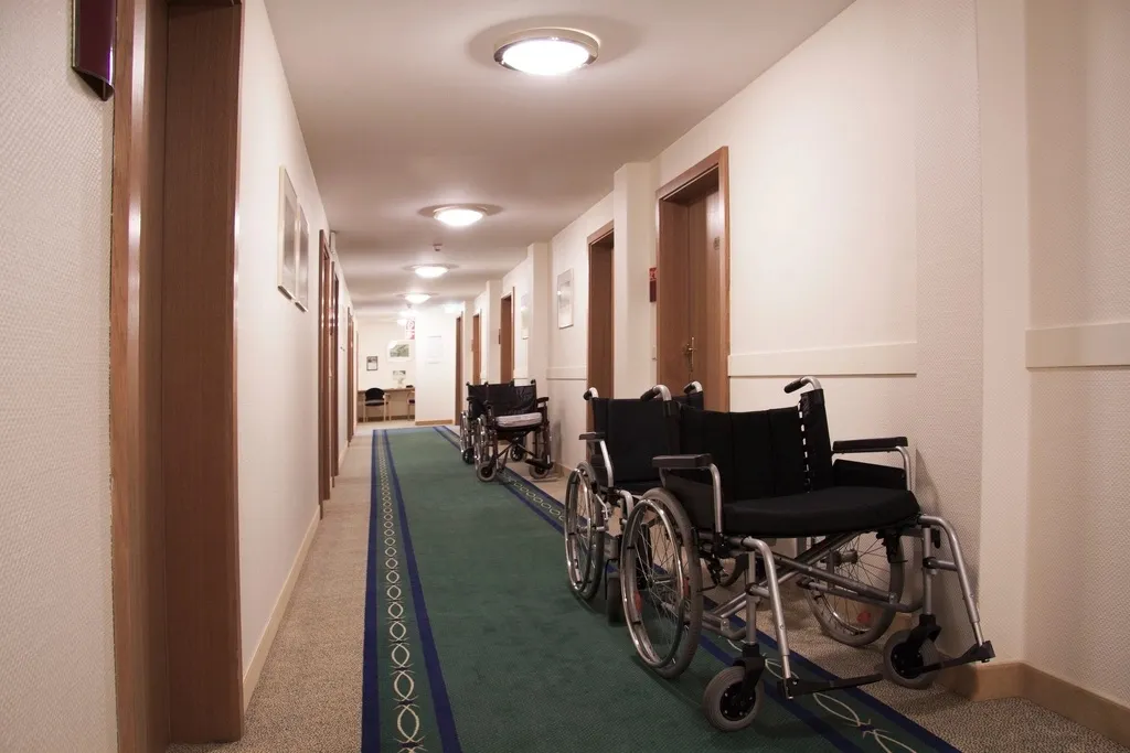 Empty manual wheelchairs lined up along the wall of a quiet carpeted hallway with closed doors