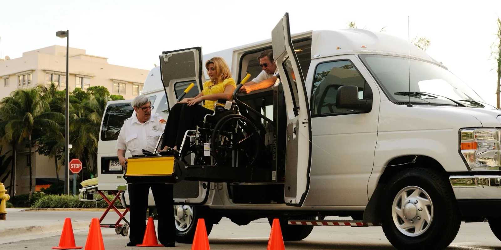A woman in a wheelchair rides the lift into a white wheelchair van while two attendants help