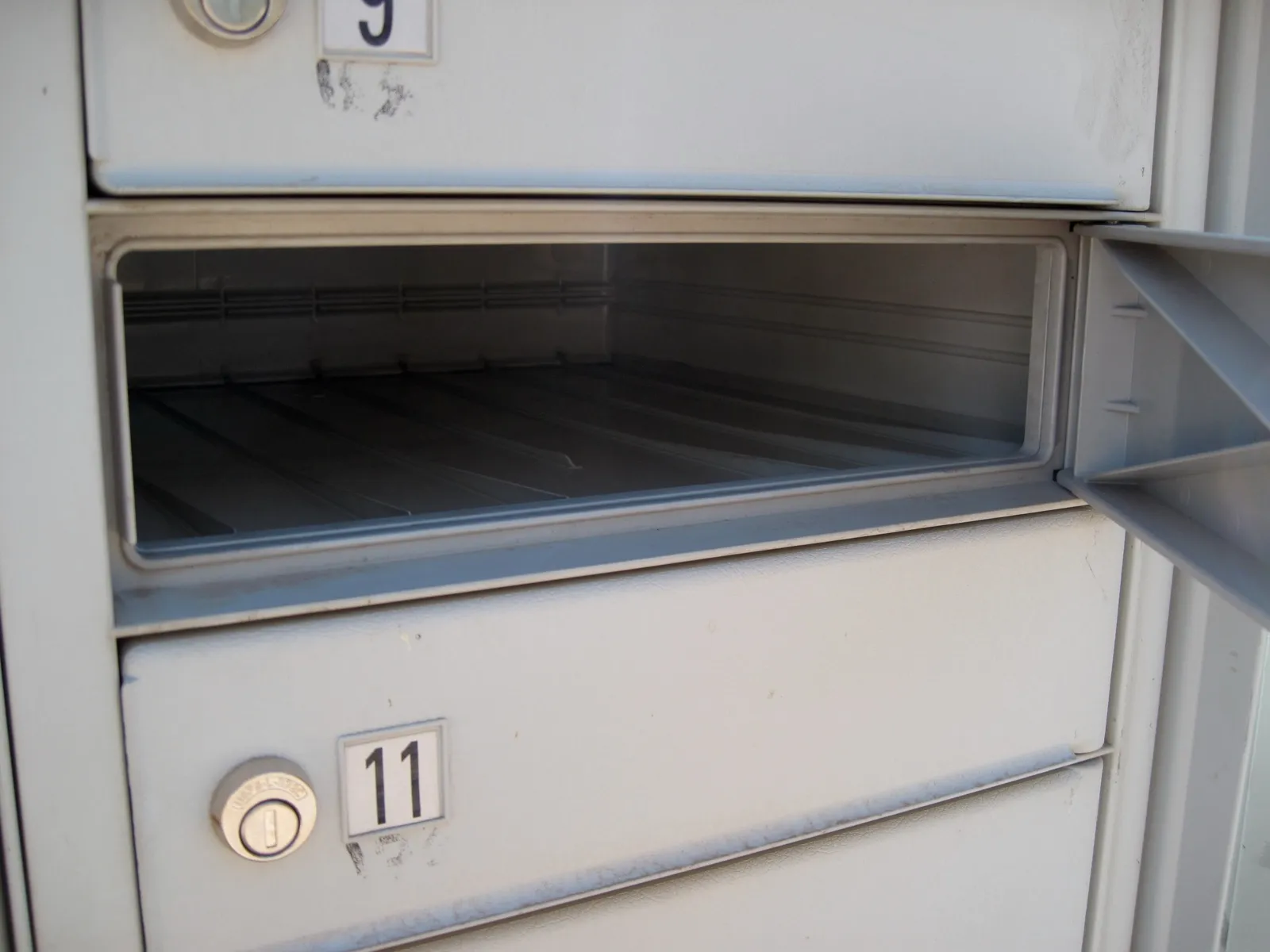 An open, empty metal mailbox in a row of numbered mailboxes