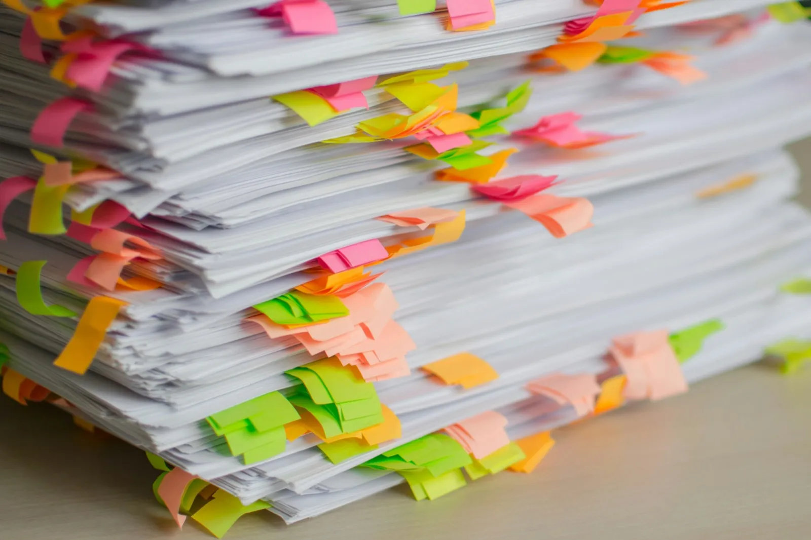 A tall stack of printed pages marked with dozens of pink, orange, yellow, and green sticky tabs on a desk