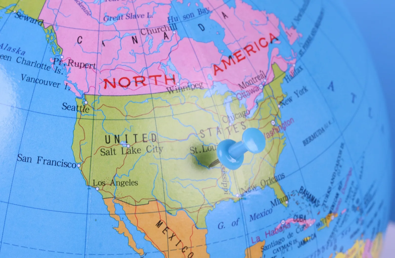A blue pushpin stuck into the middle of the United States on a colorful desk globe