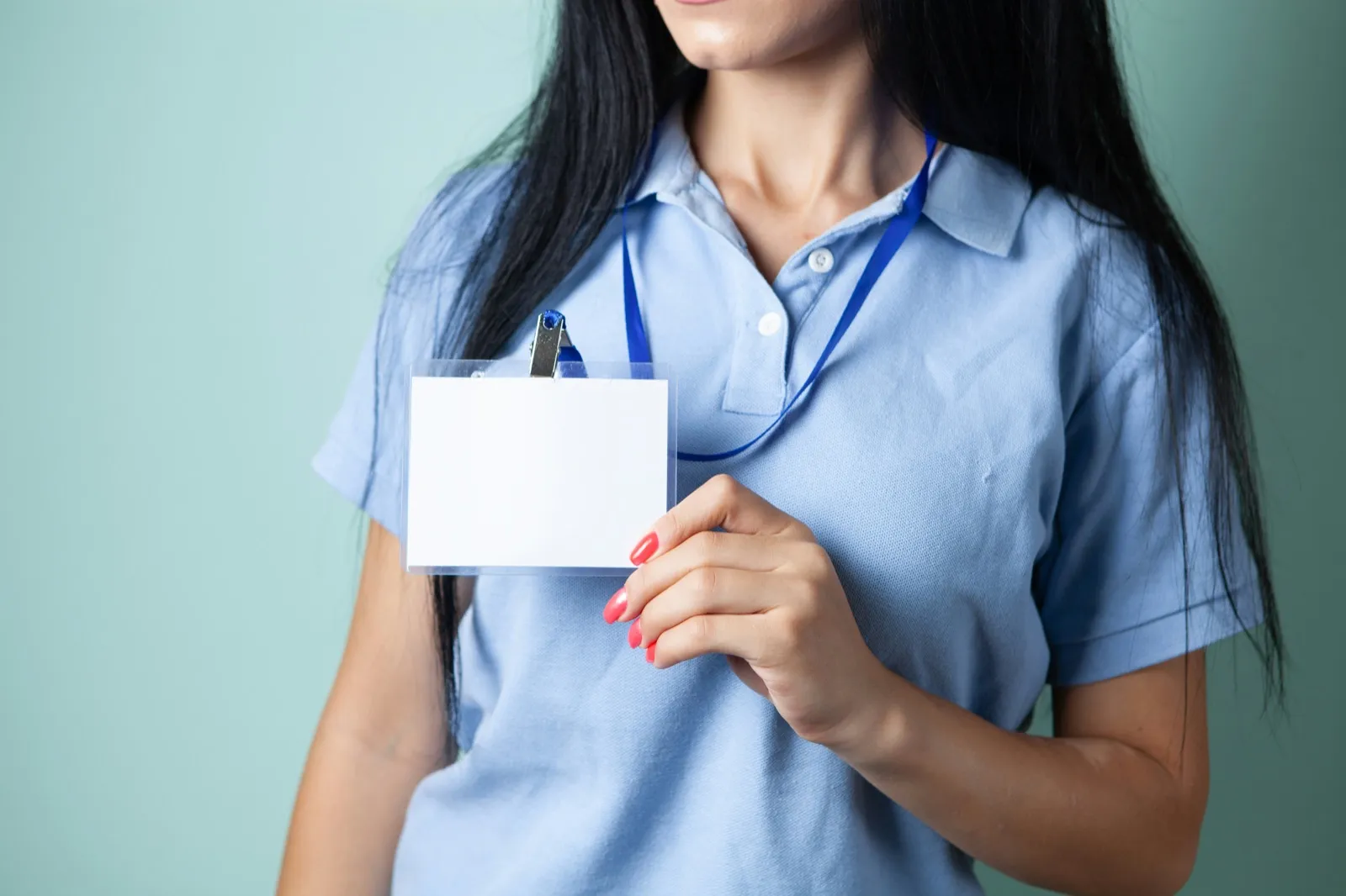 A worker in a light blue polo shirt holds up a blank white ID badge clipped to a blue lanyard