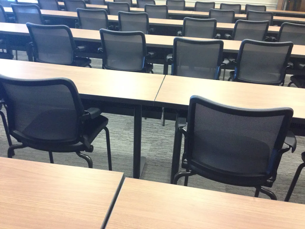 Rows of empty tables and black mesh chairs set up in a meeting room before a session