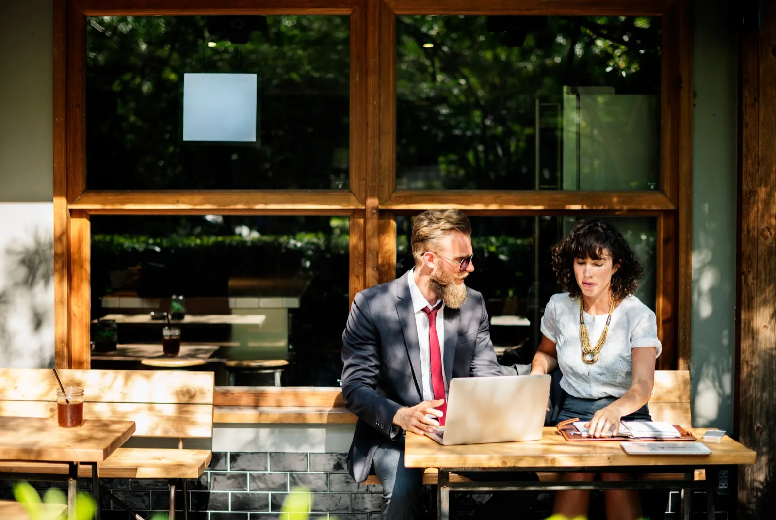 A man in a suit and a woman go over a planner and a laptop together at an outdoor cafe table