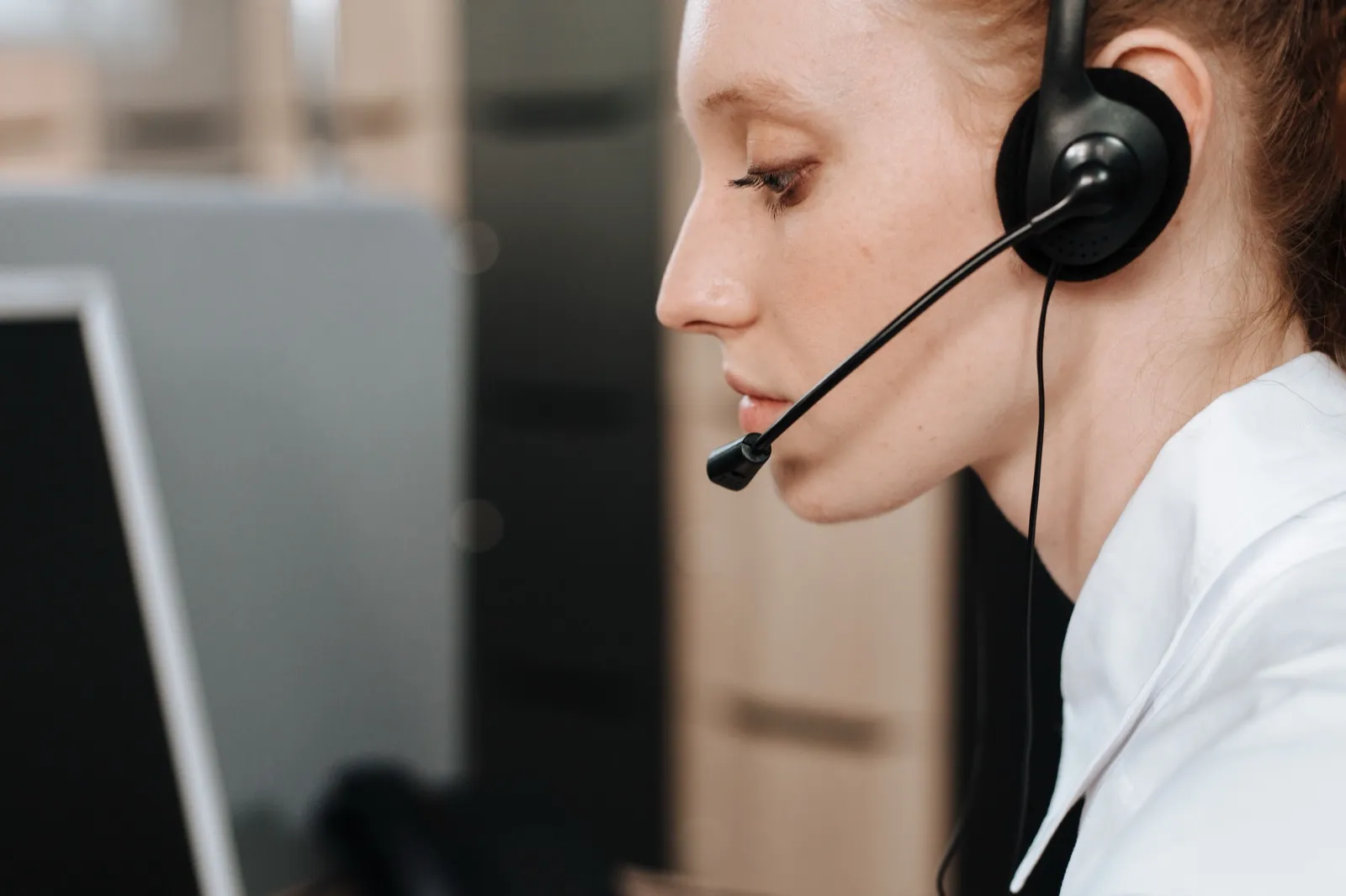 A dispatcher wearing a headset with a microphone, looking at a computer screen at her desk