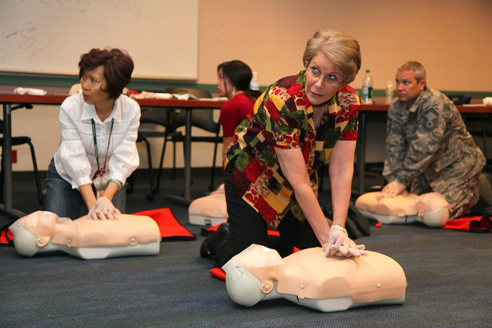 Adults kneeling on a classroom floor practicing chest compressions on CPR training mannequins