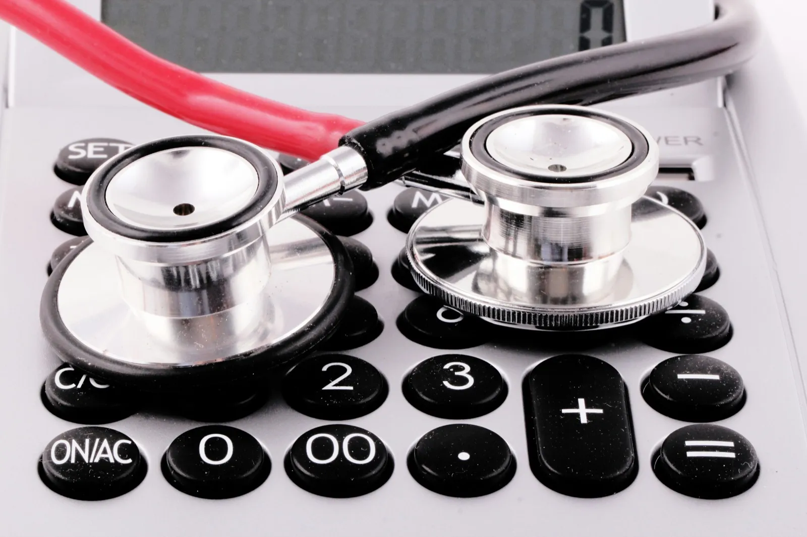 A stethoscope with red and black tubing resting on the keys of a gray desk calculator