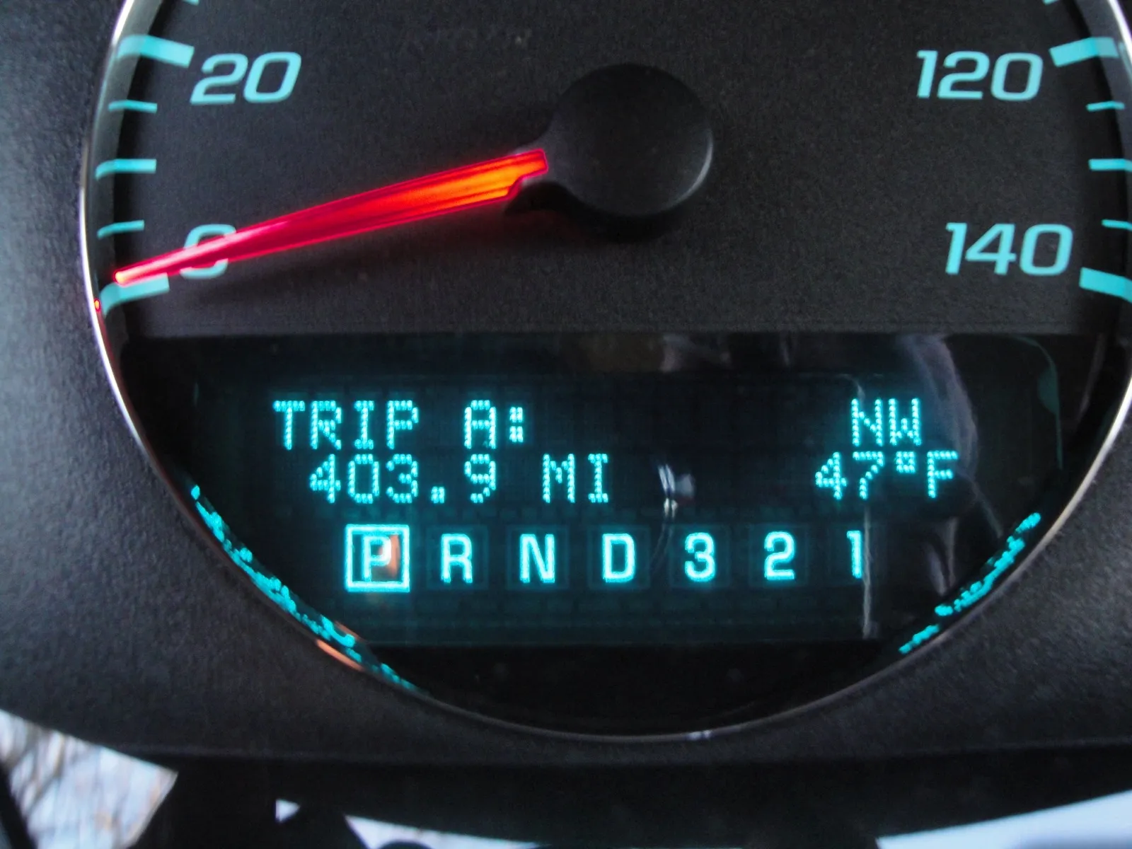 A car dashboard display lit in teal showing a trip odometer reading of 403.9 miles below the speedometer