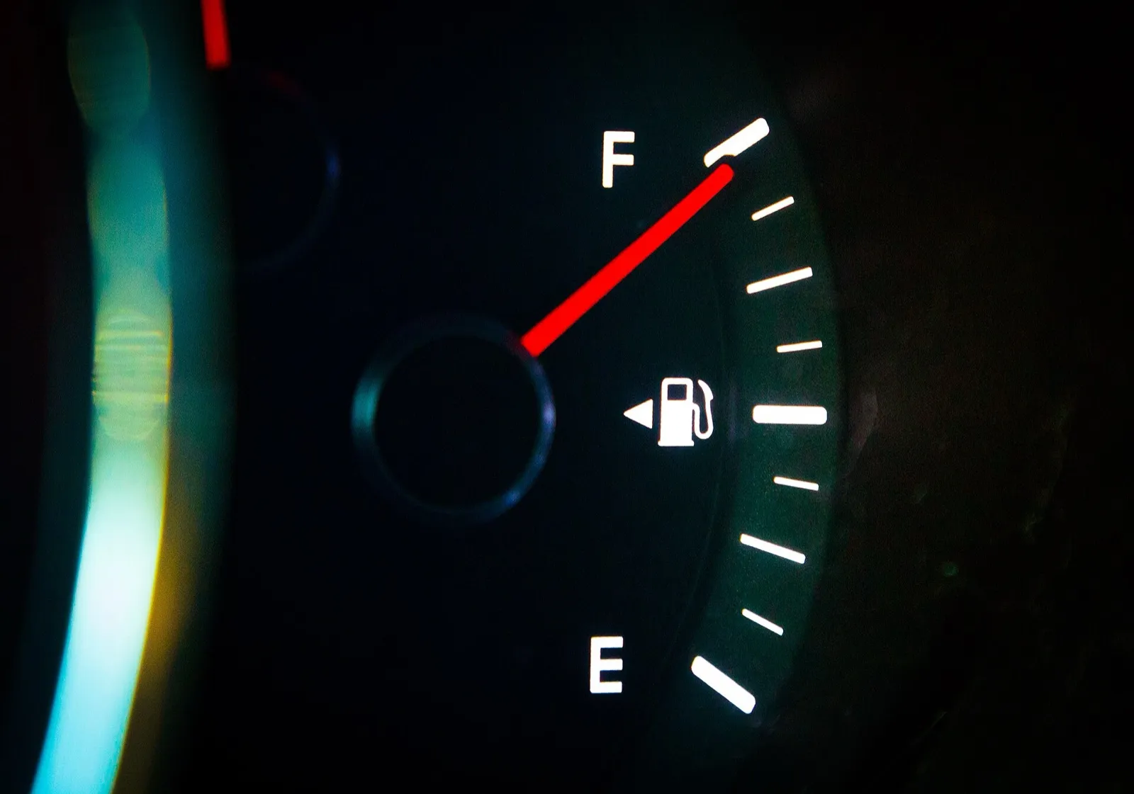 A lit car fuel gauge at night with its red needle pointing to full