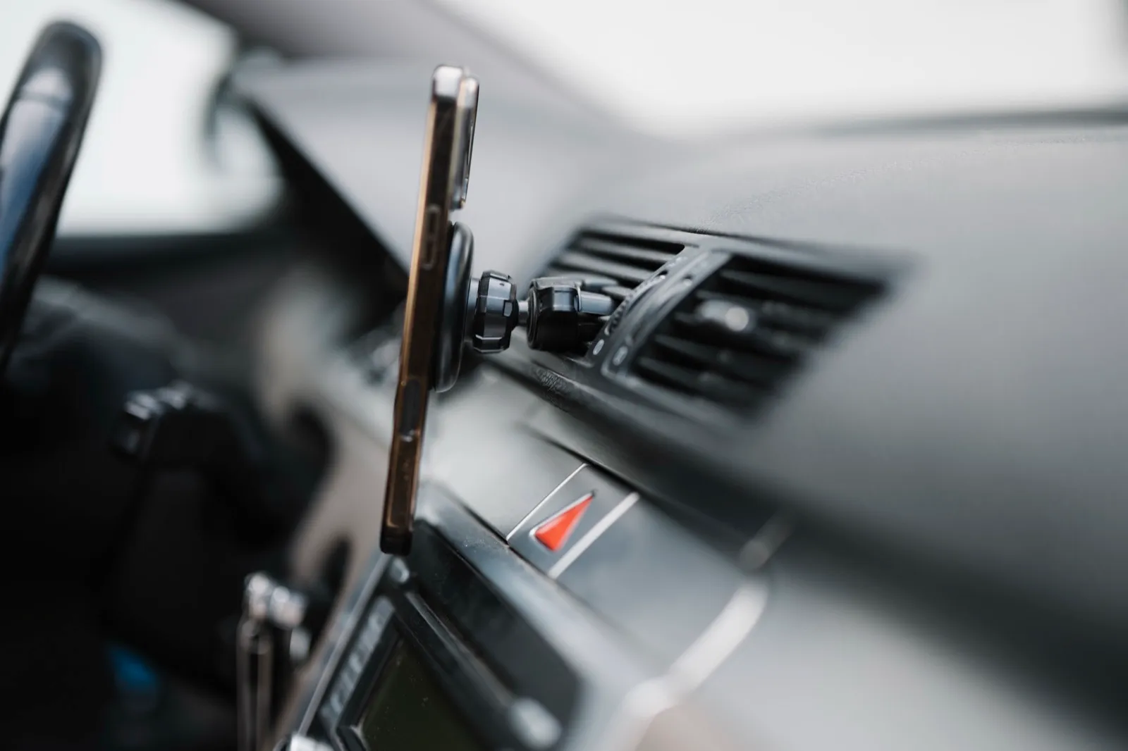 A smartphone held in a mount on a car dashboard air vent, next to the steering wheel