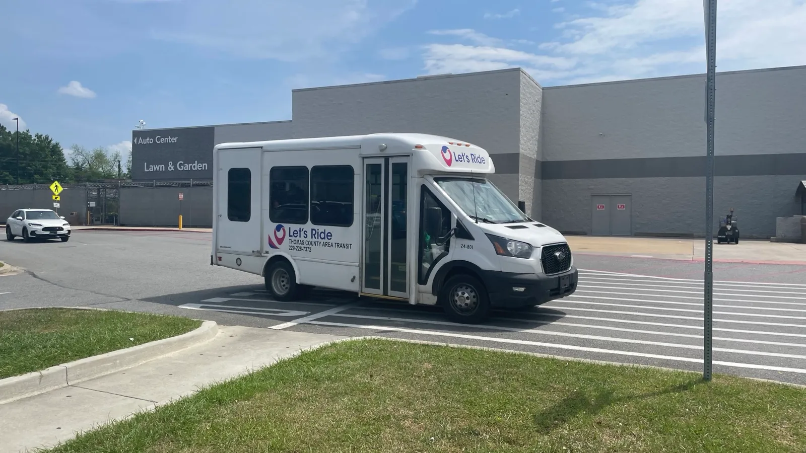 A white county transit cutaway bus with a rear wheelchair door crossing a parking lot in Thomas County, Georgia