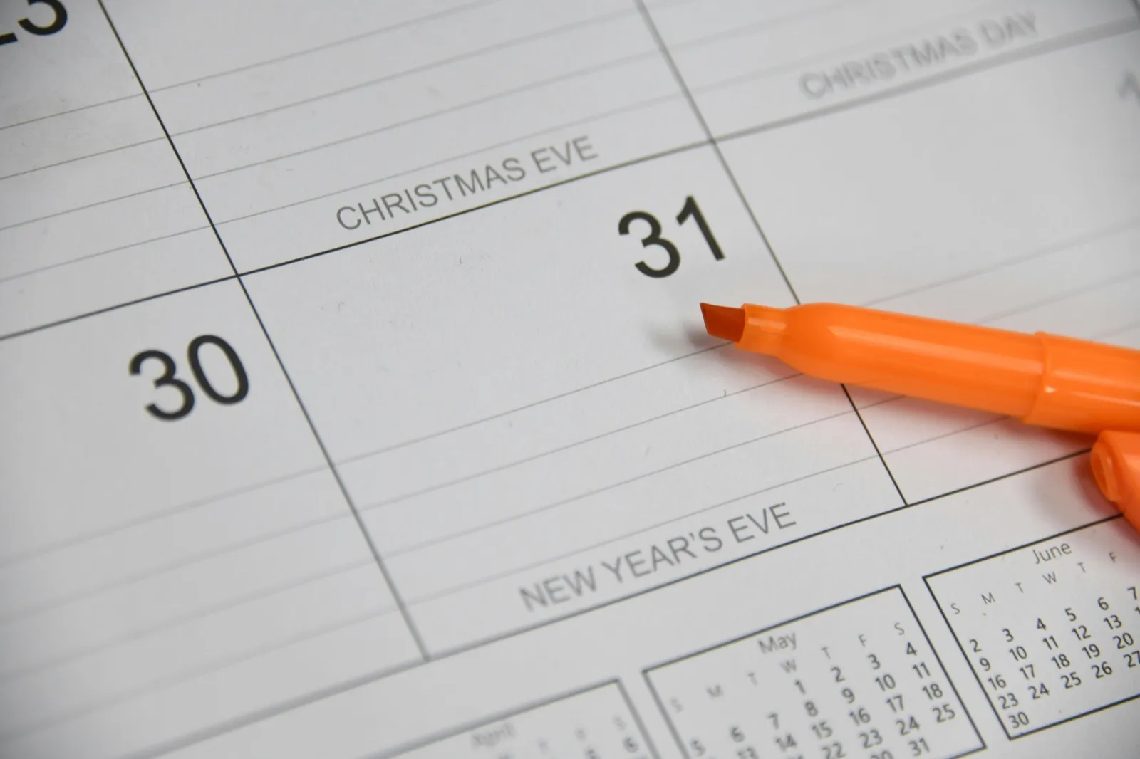 A paper calendar showing Christmas Eve, Christmas Day, and New Year's Eve, with an orange highlighter resting on it