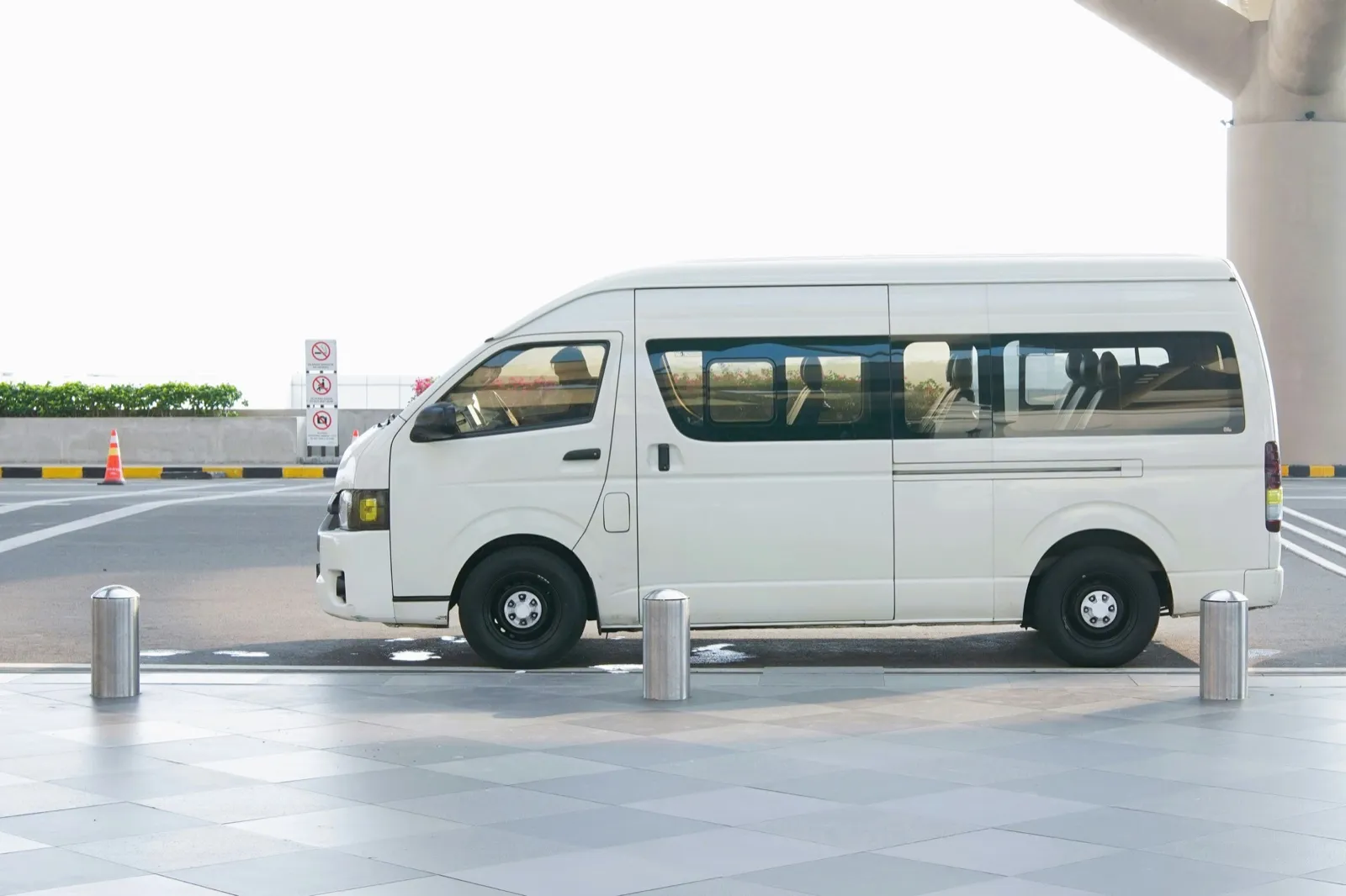A white passenger van with side windows parked at a curbside drop-off zone