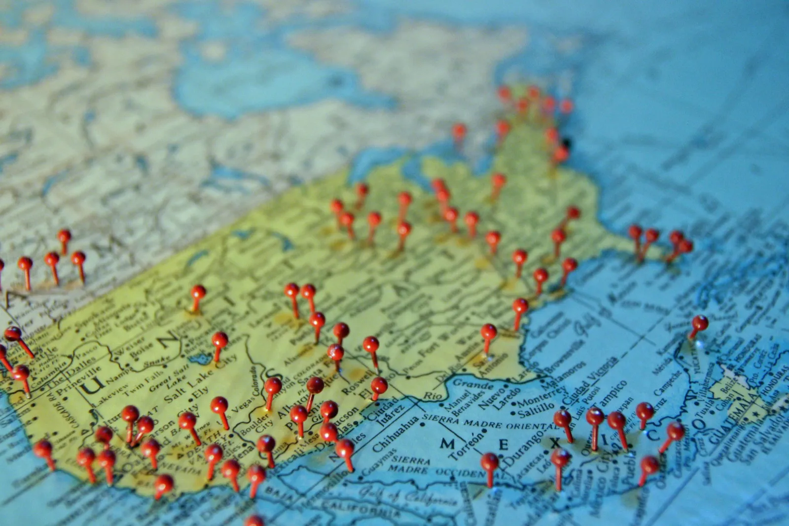 Red pushpins stuck into an old paper map of the United States and Mexico