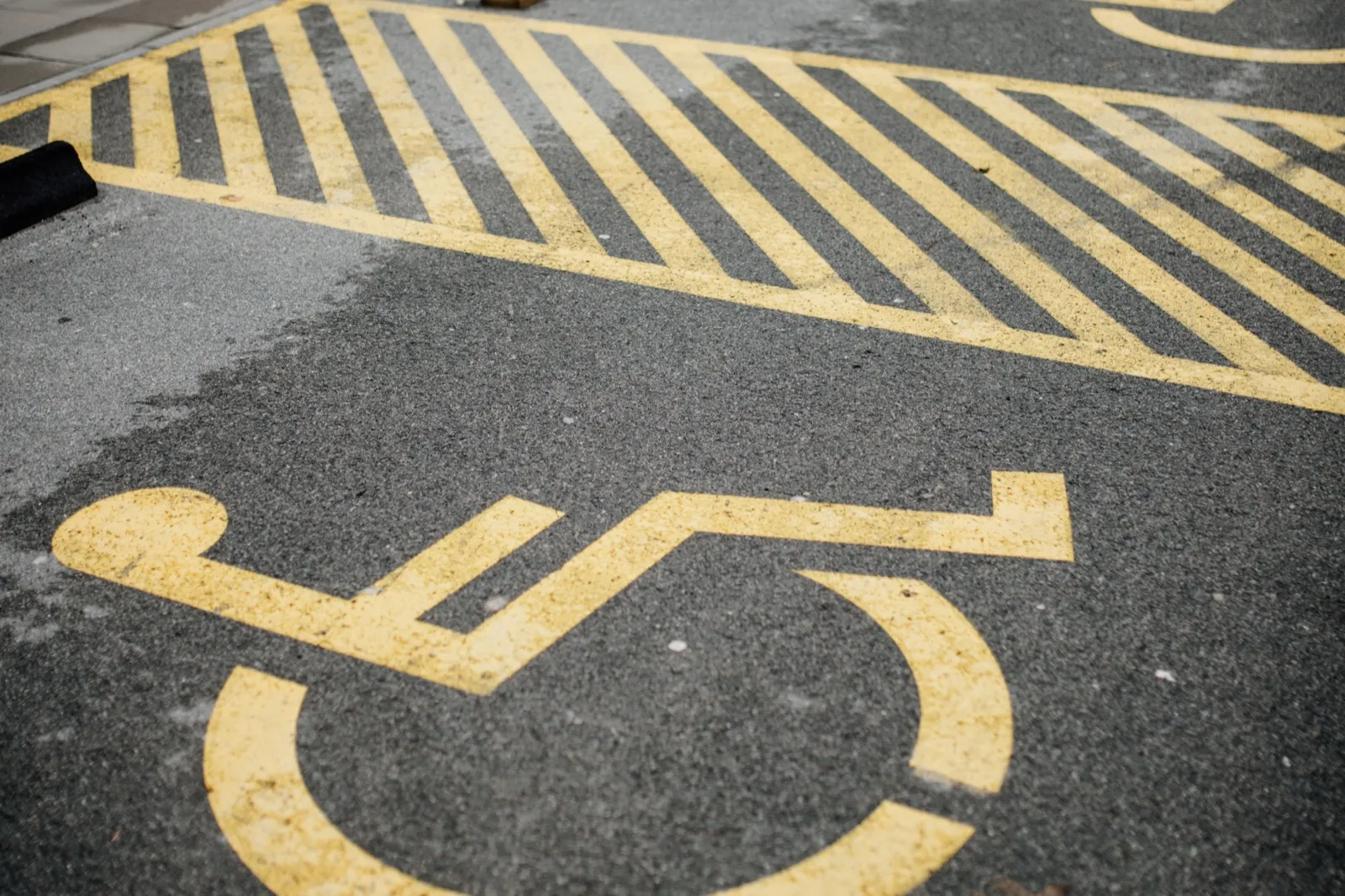 A yellow wheelchair symbol and a striped access aisle painted on the asphalt of a parking lot
