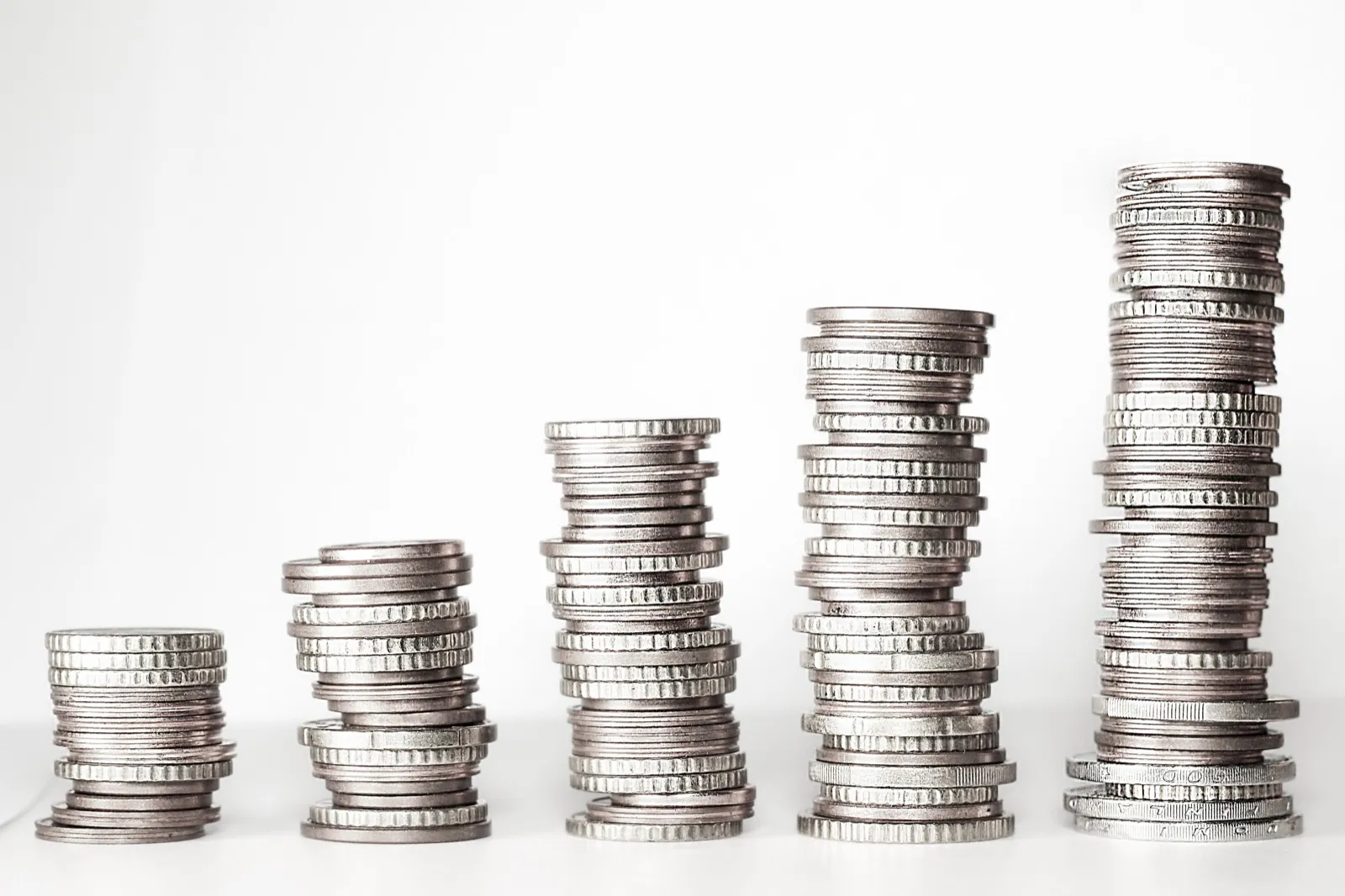 Five stacks of coins of rising height lined up on a white table