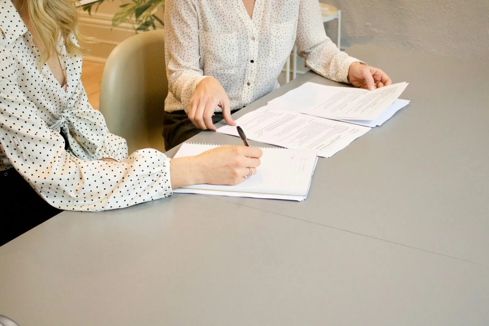 Two coworkers at an office table going over printed pages while one of them signs a notepad